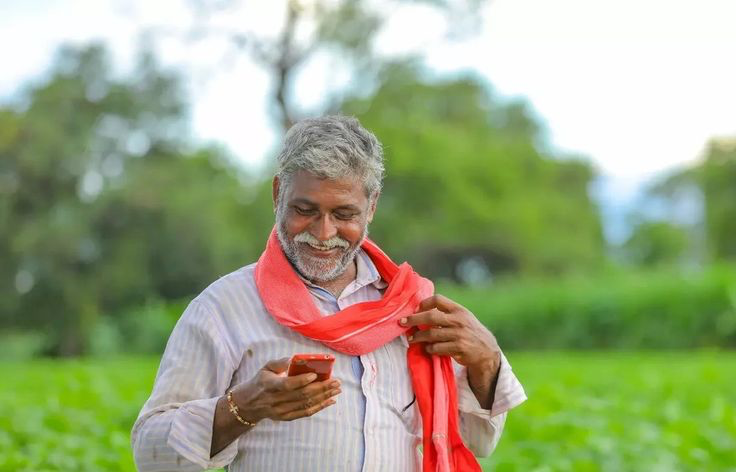 A farmer smiling while using his phone in a green field
